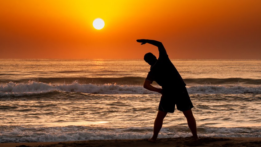 Silhouette of young man doing fitness exercise on the beach at sunrise or sunset.