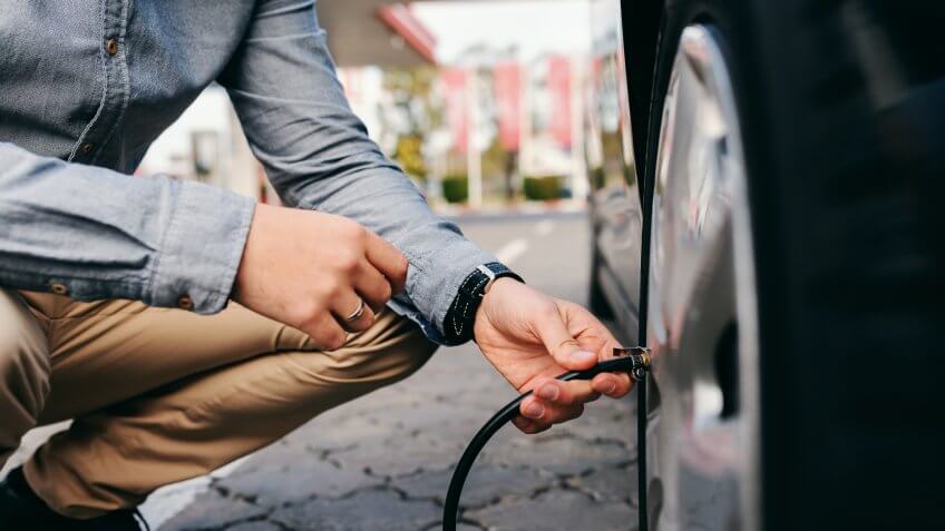 Close up of man crouching on the gas station and inflating tire.