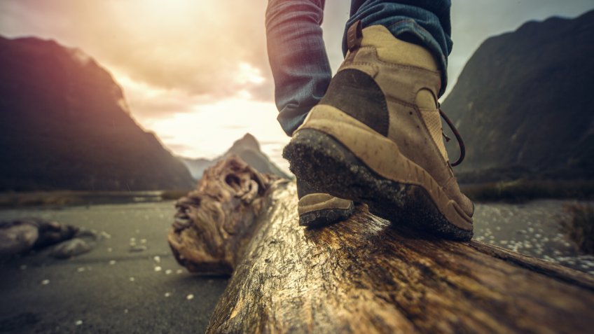 Low angle view of man's legs and hiking boots standing on tree log.