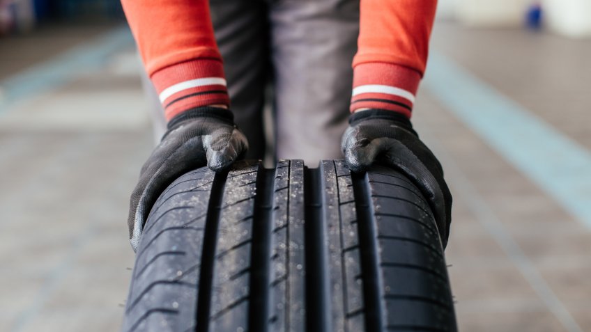 Closeup of mechanic hands holding a black tire in the workshop.