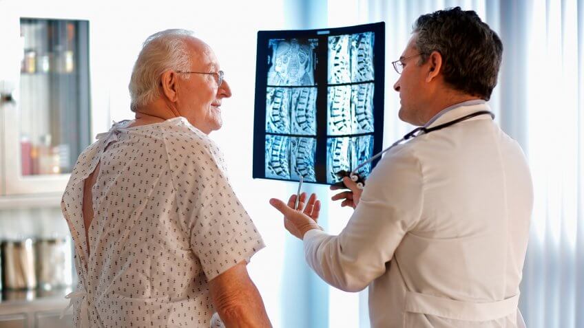 Doctor talking to senior male patient while holding up MRI.