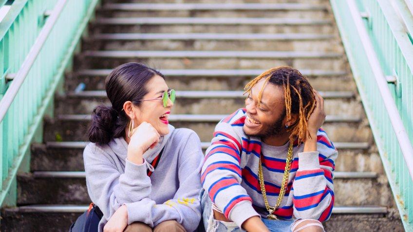 A heterosexual couple sitting outside on a sunny day, looking cheerful.