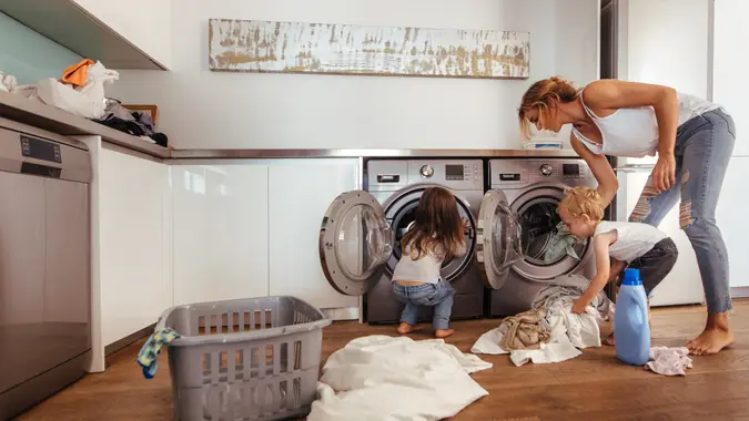 Woman with kids load clothes in washing machine.