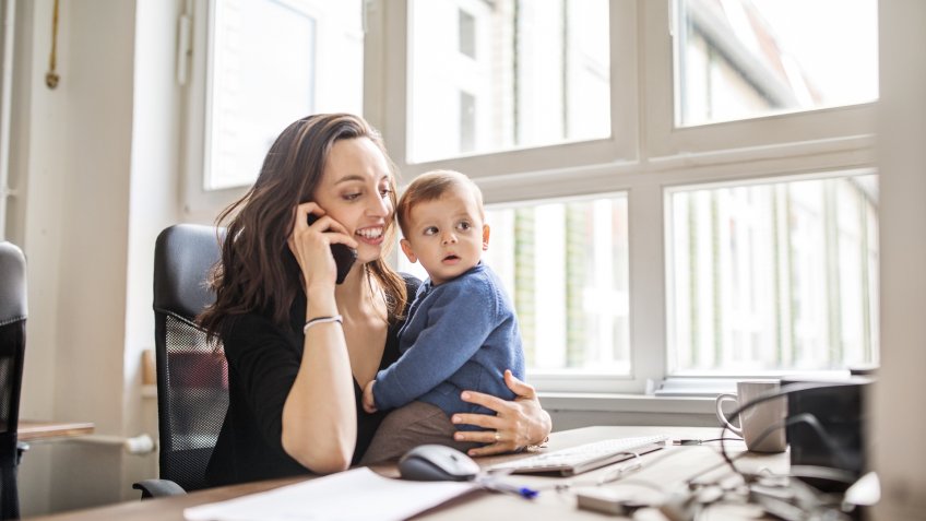 Young woman sitting at table with her son talking on mobile phone in office.