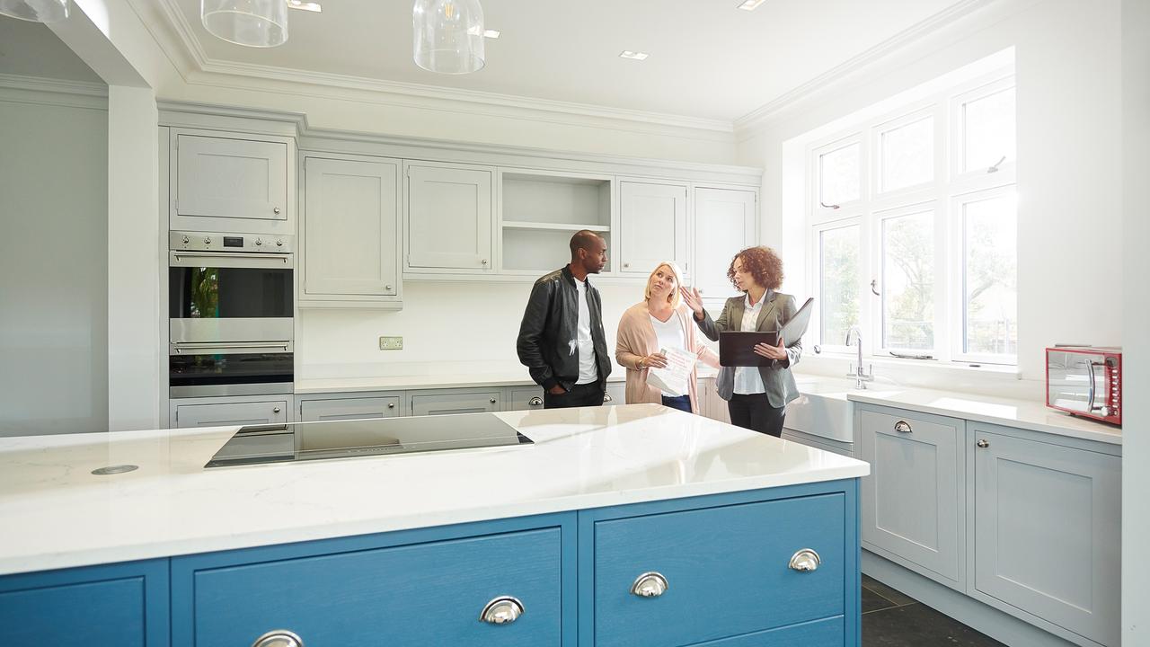 a saleswoman or estate agent shows a couple around a home with new kitchen.