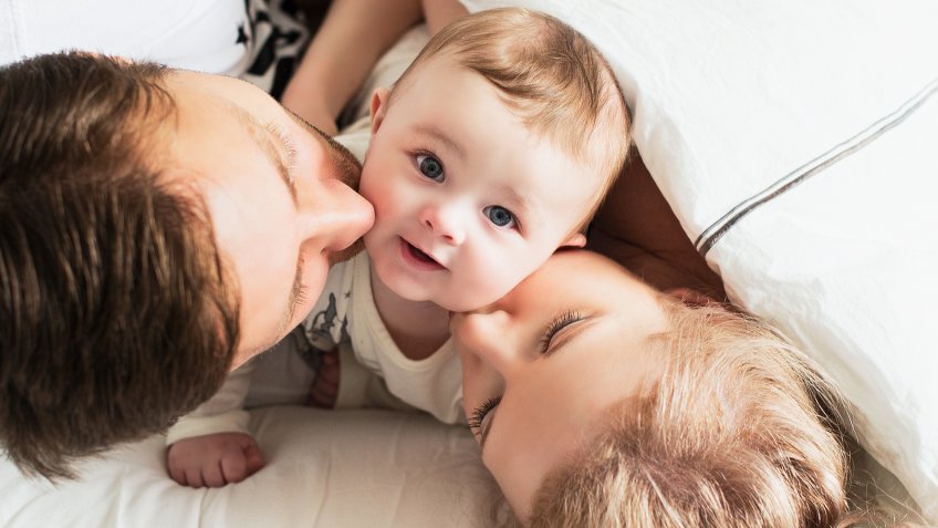 Parents kissing their baby - Image.