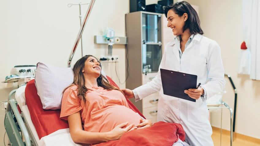 Pregnant woman lying down on a hospital bed and talking to a doctor.