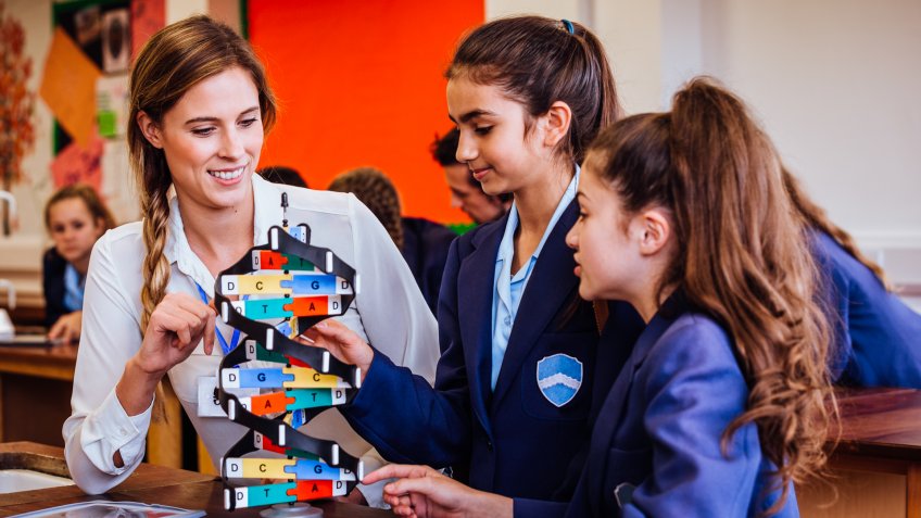 Two girls with their female teacher sat at a table in the science lab using a helix model.