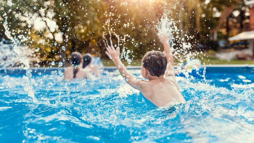 Photo of Three Caucasian happy children playing and splashing on the swimming pool at the day time.