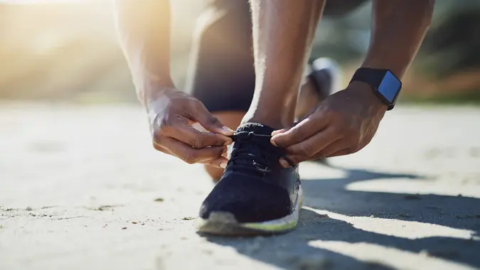 Closeup shot of an unrecognizable man tying his shoelaces while exercising outdoors.