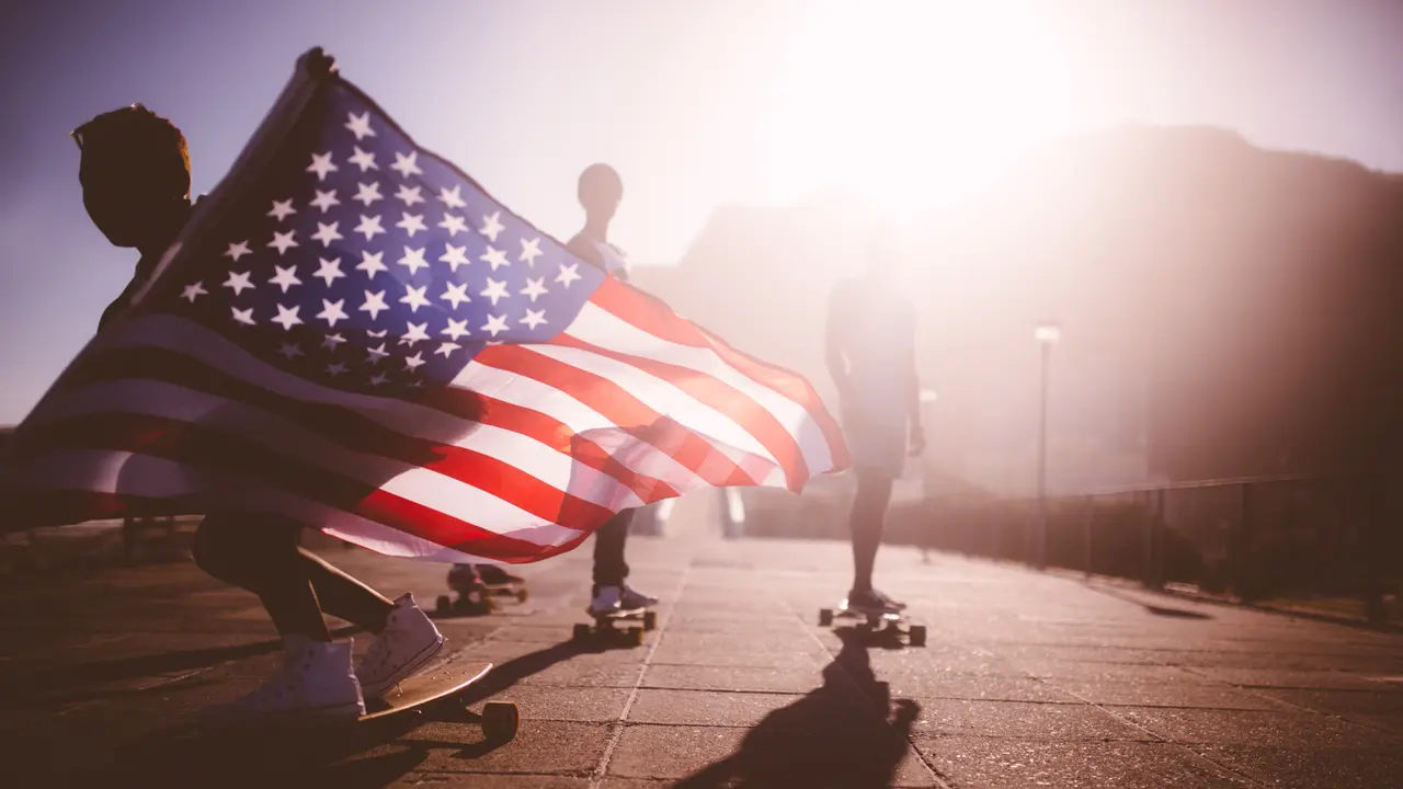 Teenage African American skater flying an American flag past the camera.