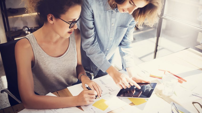 two women coworkers talking over tablet