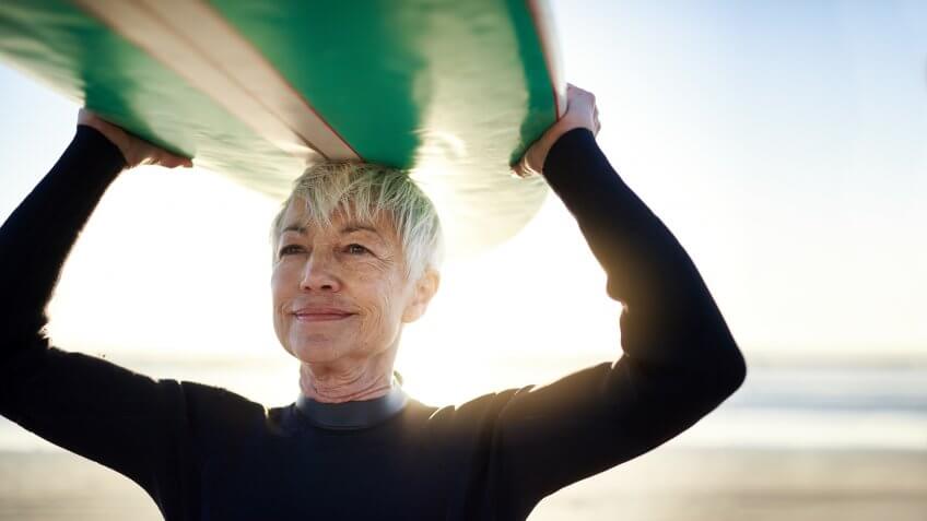 Cropped shot of a senior woman holding a surfboard on top of her head on her way to go surfing.