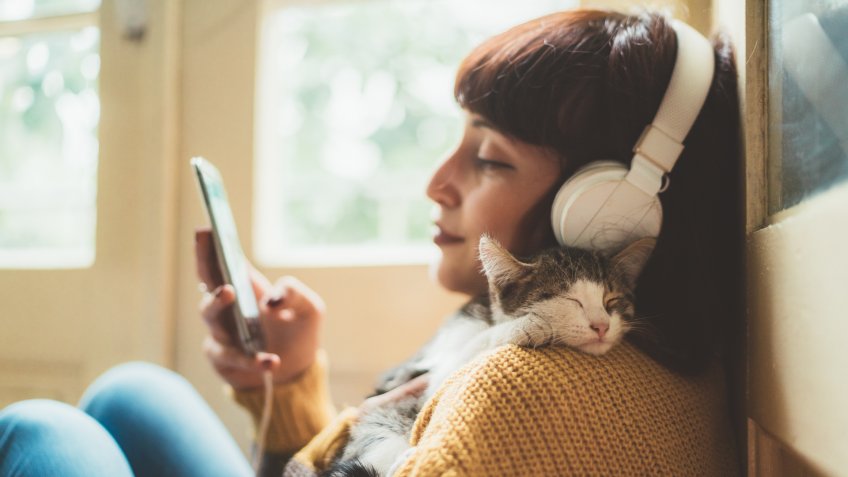 Woman at home listening to music and cuddle her cat.