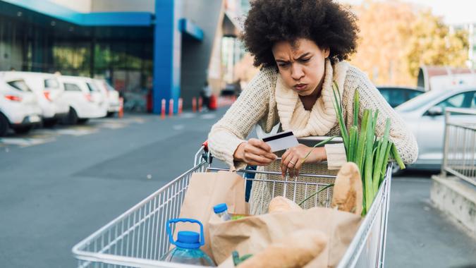 Woman pushing shopping cart and looking at credit card.
