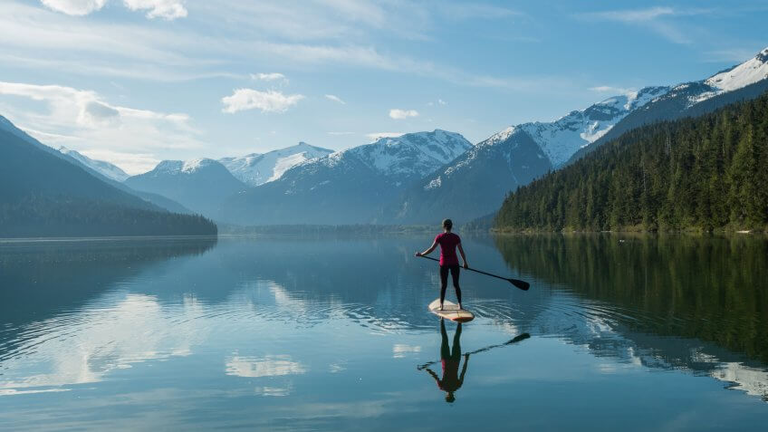 Woman stand up paddle boarding on a pristine mountain lake.