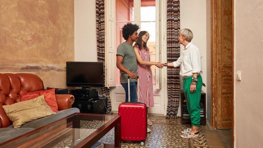 Full length of happy young woman standing by man shaking hands with female realtor.