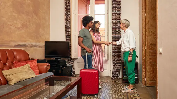 Full length of happy young woman standing by man shaking hands with female realtor.