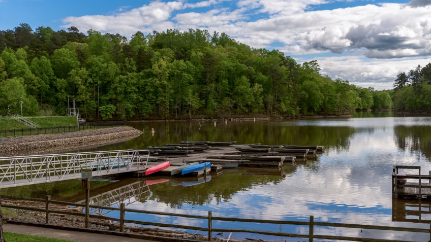 Walkway leading to dock on a lake with upside down canoes with sky and clouds in the background - Image.