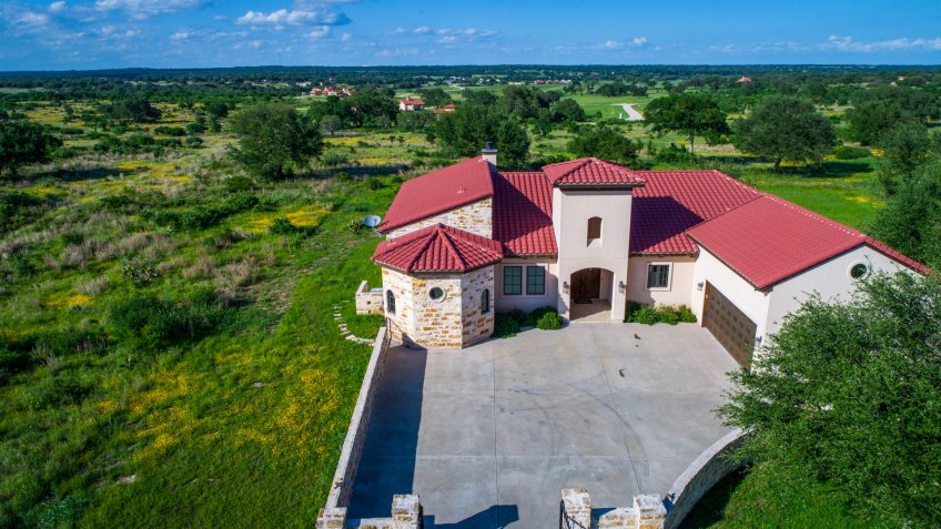 Aerial drone view above green landscape Luxury mansion home on vineyard winery open green Texas hill country landscape with Spanish architecture and large concrete courtyard.