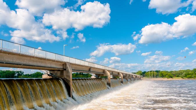 The waters of the Mississippi River flow briskly over the Coon Rapids Dam just outside of Minneapolis, Minnesota on a sunny summer day with blue skies and white clouds.