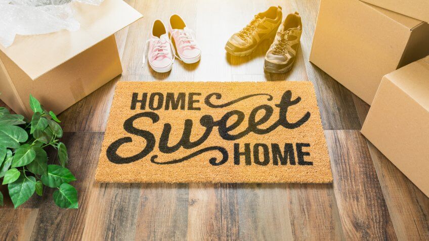 Home Sweet Home Welcome Mat, Moving Boxes, Women and Male Shoes and Plant on Hard Wood Floors.