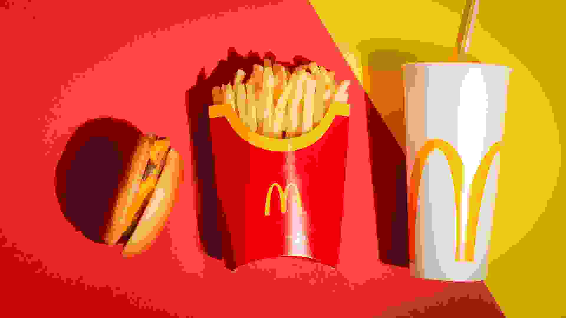 McDonalds cheeseburger fries and drink on red and yellow backgro