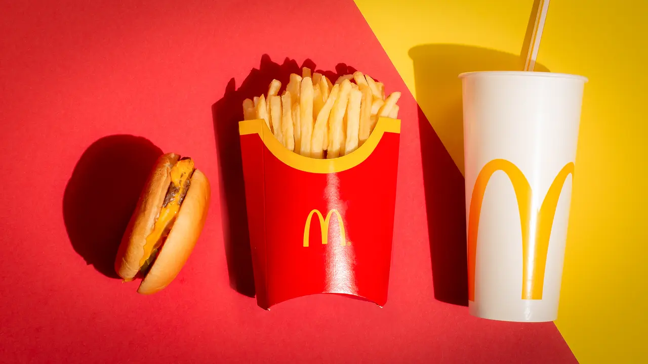 McDonalds cheeseburger fries and drink on red and yellow backgro