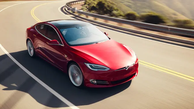 A red Tesla Model S driving on an open road on a sunny day.