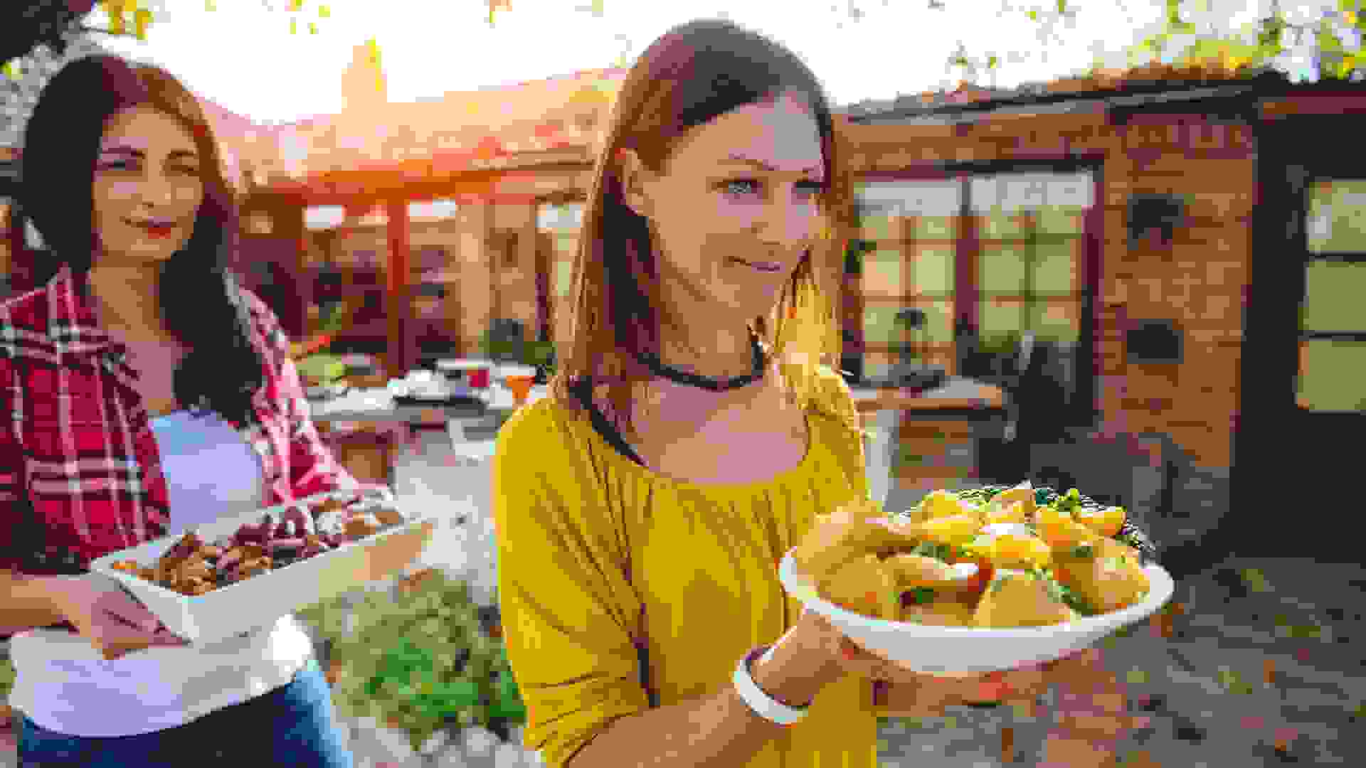 Woman carrying a bowl with roasted potatoes at backyard patio.