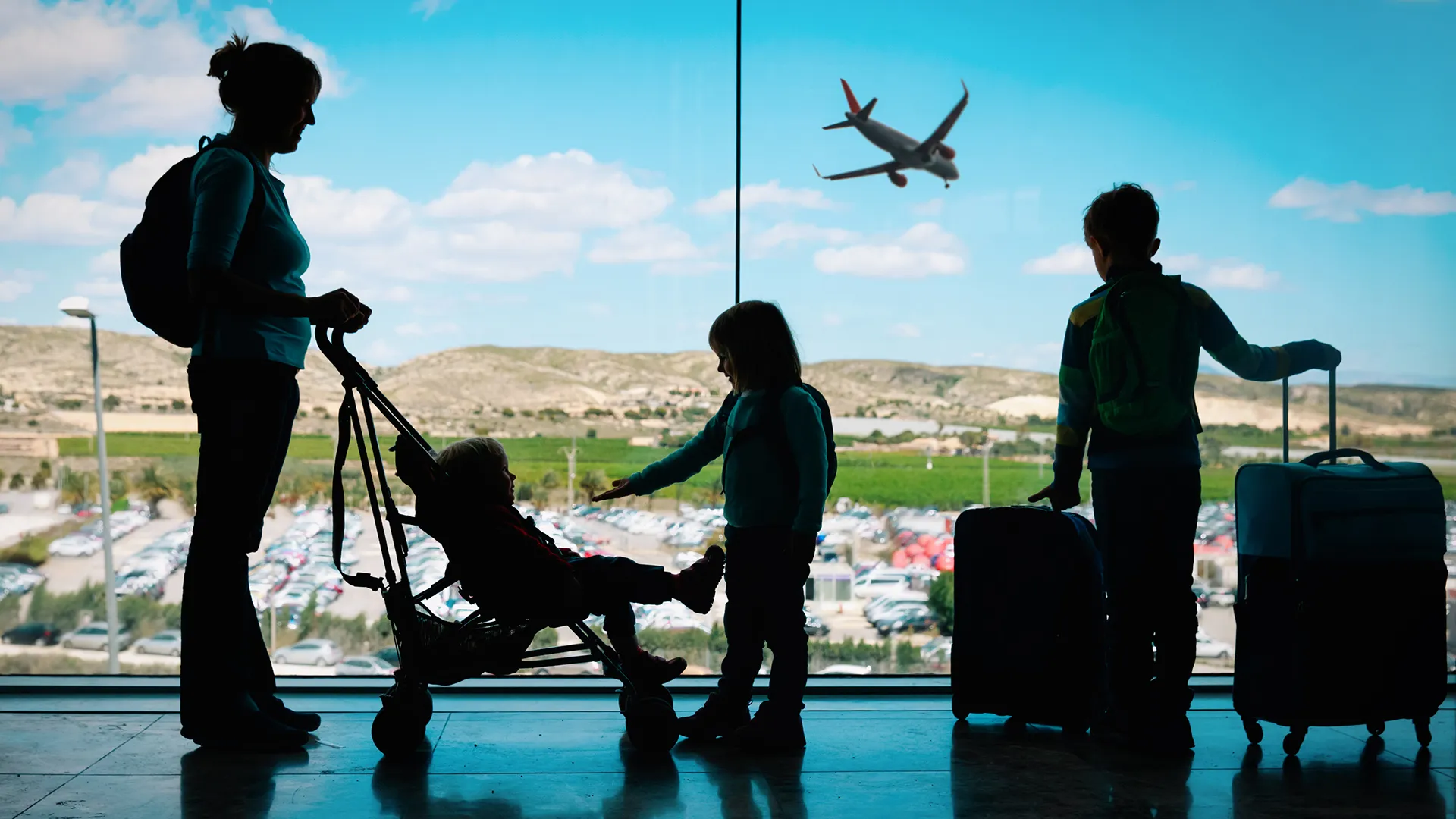 mother with kids and luggage looking at planes in airport, family travel.