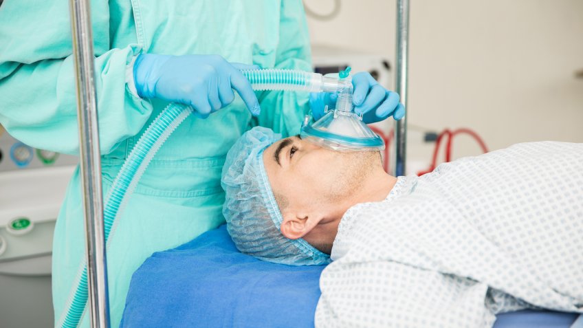 Profile view of a male patient lying on a hospital bed and being put to sleep with anesthesia before surgery.