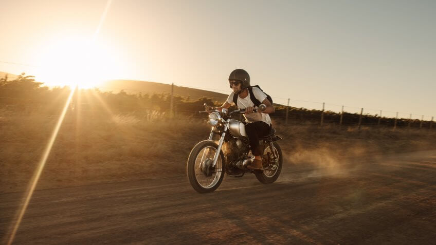 Male biker driving a vintage motorcycle on dirt road.