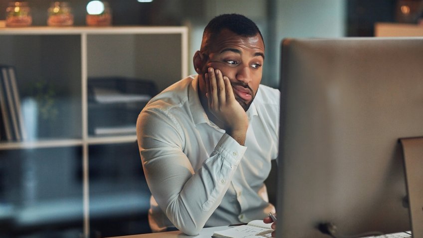 Shot of a young businessman looking bored while working at his desk during late night at work.
