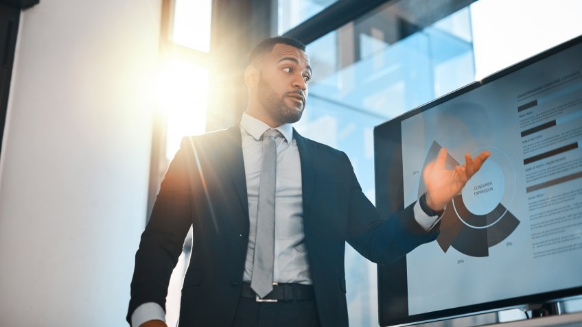 Shot of a young businessman presenting data on a screen during a meeting in an office.