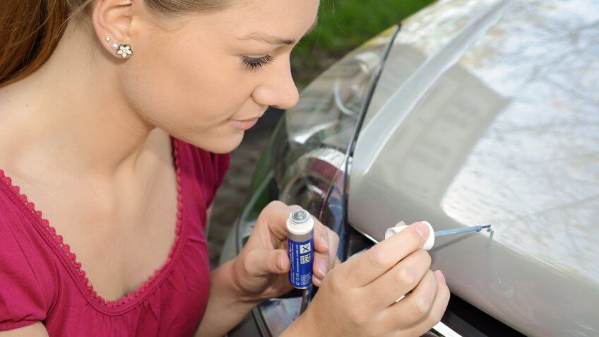 Woman repairs scratches and chips on bonnet with car paint and brush - Image.