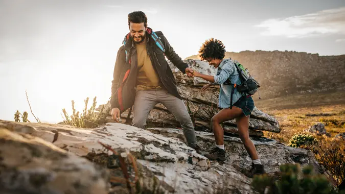 Young man helping friend to climb up the rock.