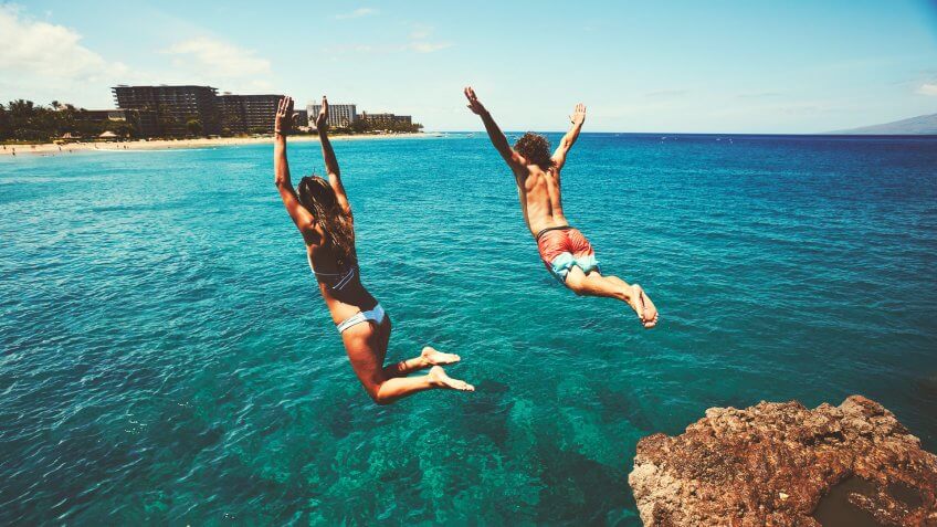 couple jumping off of cliff in ocean