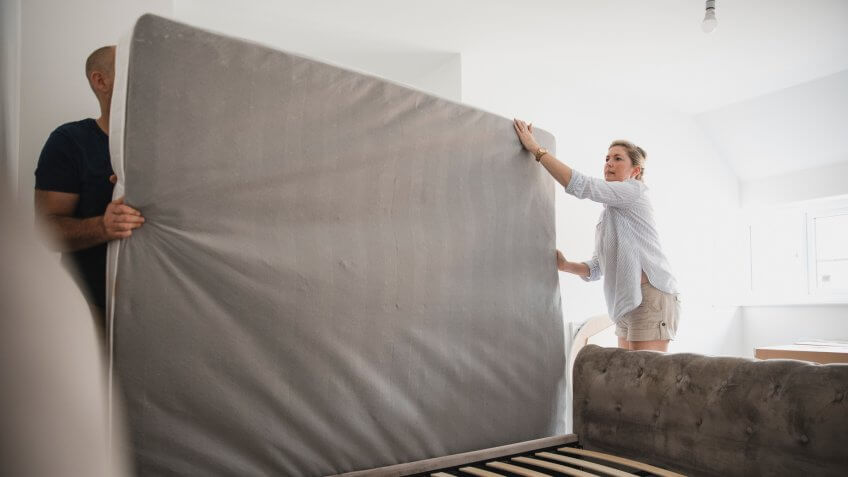 Mature couple are setting up their bed in their new home.