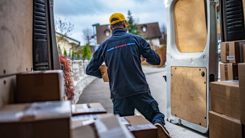 Rear view of delivery man holding parcel and walking out of van.