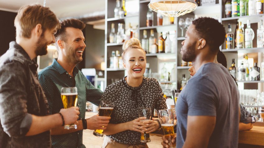 Excited multi ethnic group of friends - caucasian and afro american - gathering in the pub, talking, drinking beer.