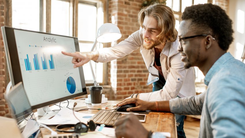 Two male coworkers working with analitycs in the beautiful office with brick wall on the background.