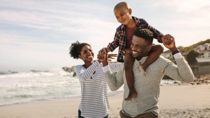 Parents carrying son on shoulders on beach vacation.