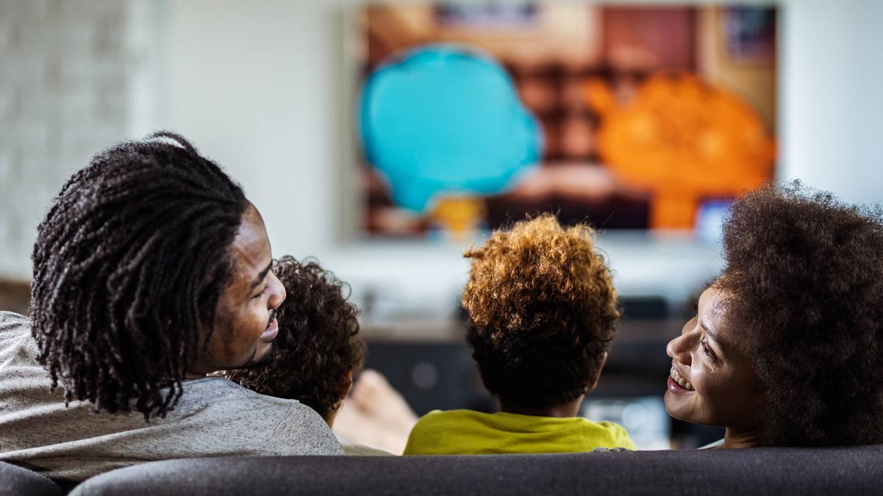 Rear view of happy African American parents communicating while watching a movie with their kids in the living room.