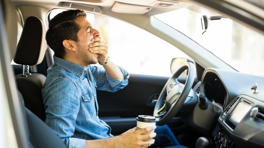 Young man feeling tired and yawning while driving a car.