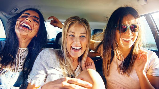 Three vivacious girlfriends on a road trip together sitting as passengers in the back of the car giggling and laughing with pleasure and enjoyment.