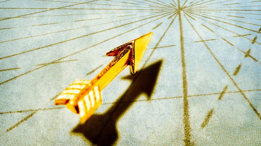 A golden arrow points toward the intersection of of navigational lines from an old world map.