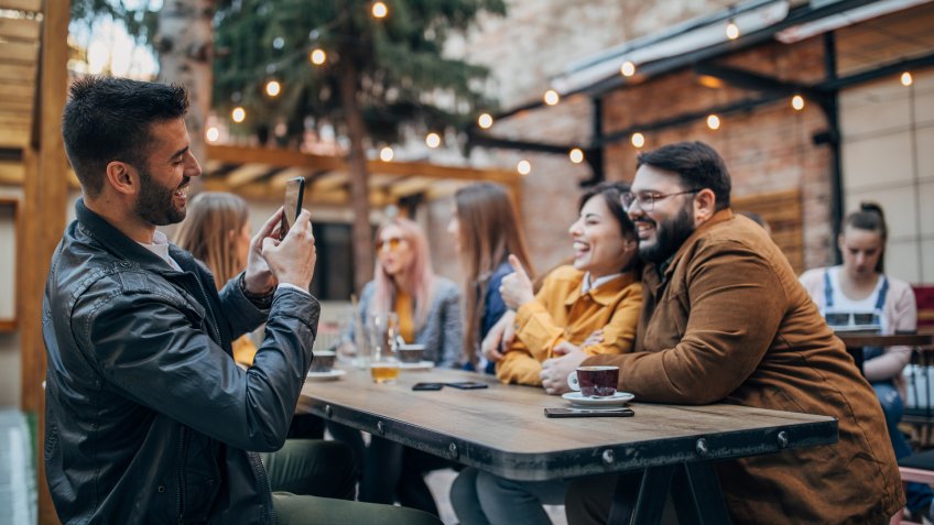 Group of people, men and women sitting outdoors in pub, having fun together.