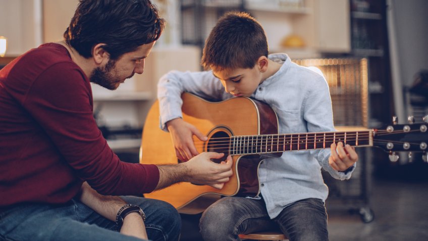 Boy teaching to play guitar in music school.