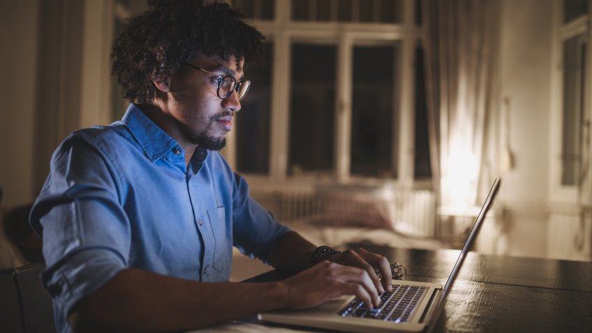 Young and determined black student studying at night at home, with a help of a laptop computer.